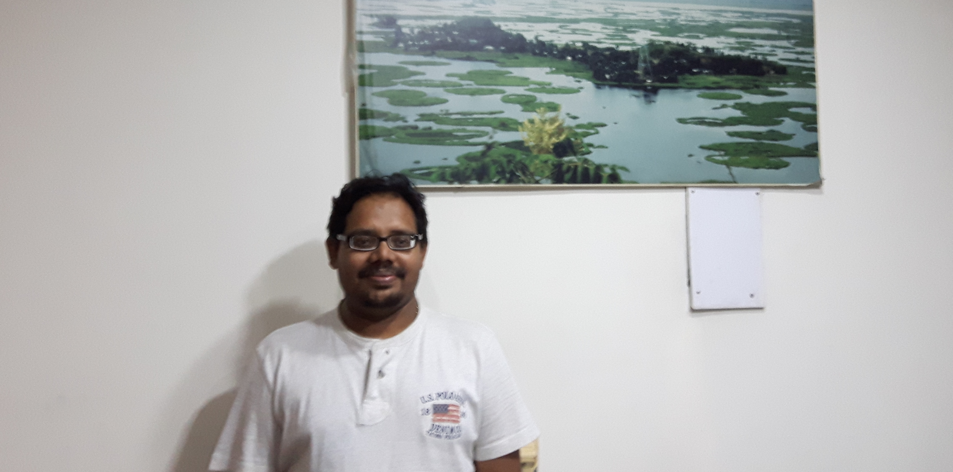 Dr. Ritesh Kumar standing in front of photo of Loktak Lake.